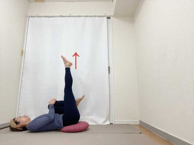 お尻の下にクッションを敷いて膝を抱えた仰向けから左脚を天井に伸ばした体勢