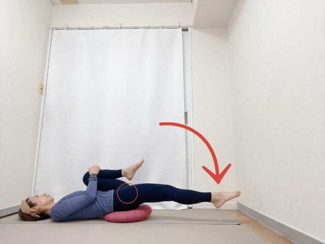 お尻の下にクッションを敷いた仰向けから右膝を抱え、左脚を伸ばした腸腰筋のストレッチ