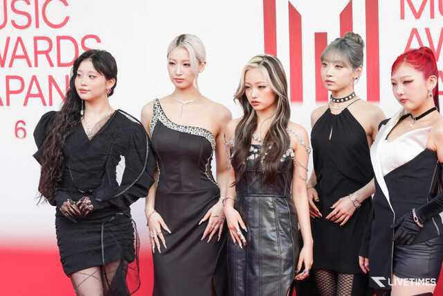 Five women in elegant black dresses posing on a red carpet with a red and white backdrop, part of an awards event show.